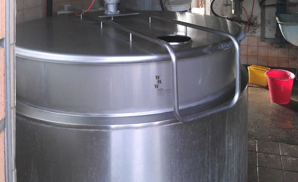 Grosser Edelstahlbehälter mit gewölbtem Deckel und Metallgriff. Daneben steht ein roter Eimer.