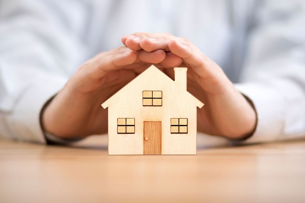 Mains protégeant une miniature de maison en bois