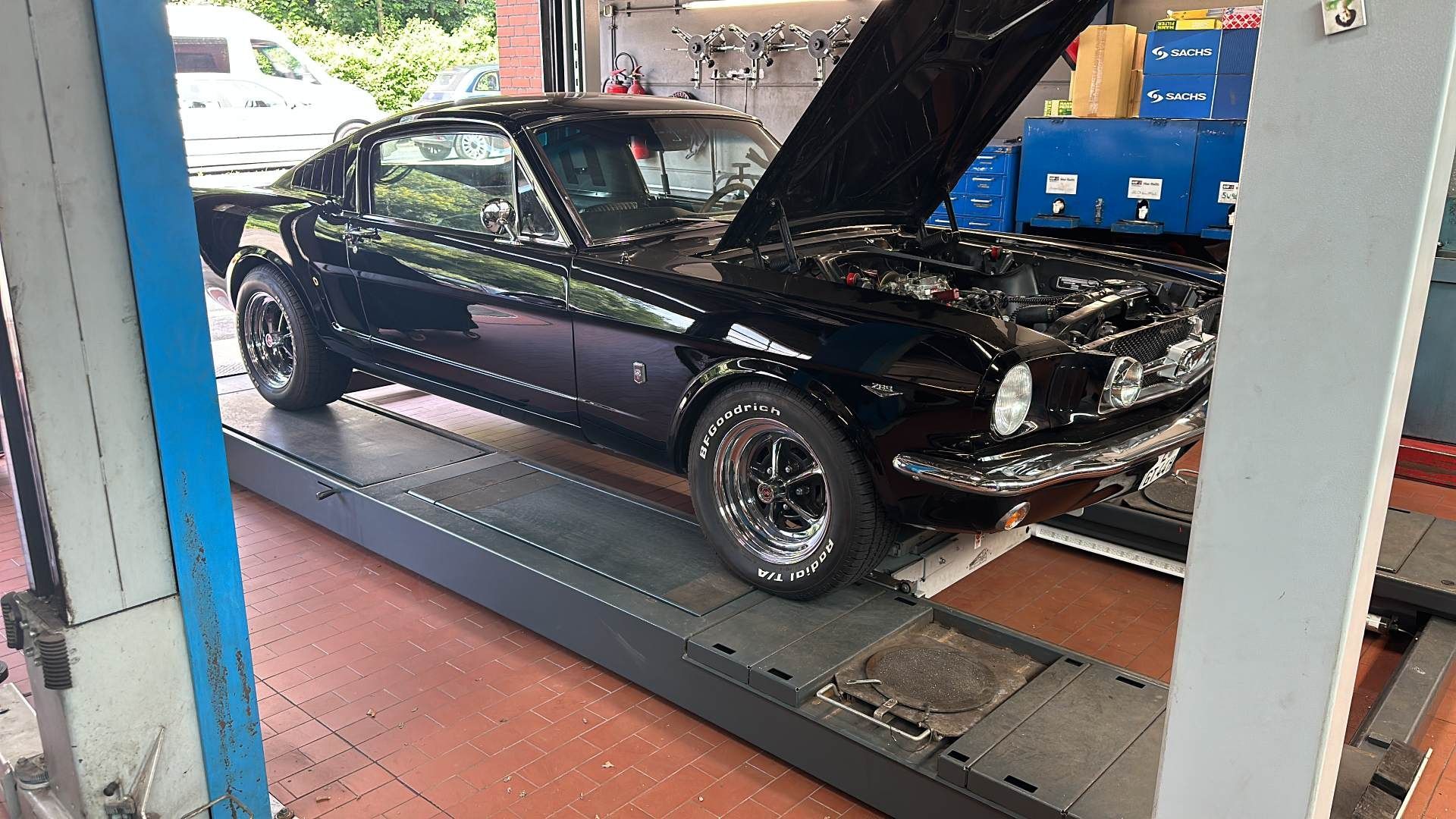 Schwarzer Sportwagen auf einer Hebebühne in einer Autowerkstatt, Motorhaube während der Wartung geöffnet.