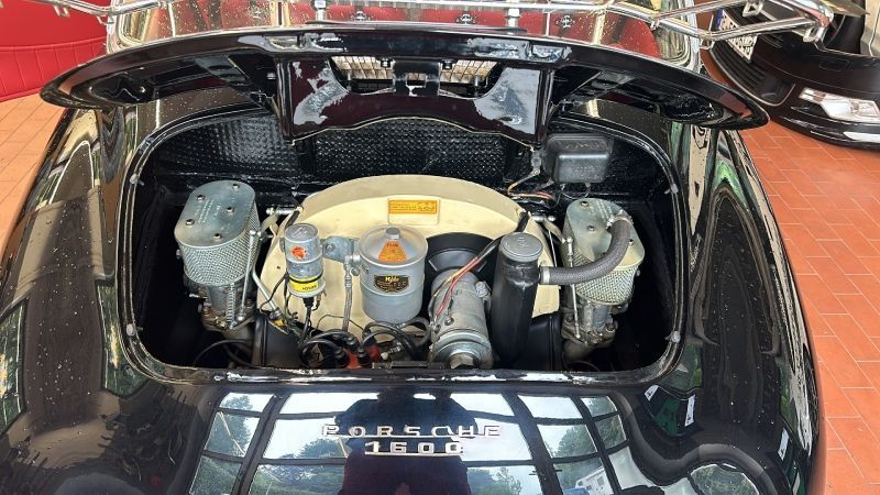 Motorraum eines Oldtimers mit geöffneter Heckklappe, der die schwarze Karosserie und silberne Motorkomponenten zeigt.