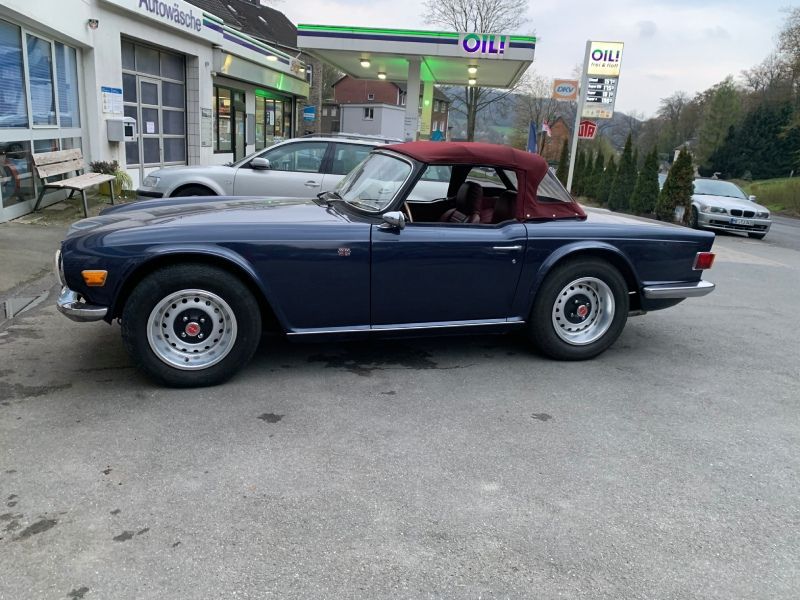 Ein blaues, klassisches Cabriolet mit rotem Verdeck und silbernen Felgen parkt vor einem Geschäft.