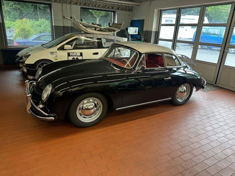 Ein klassisches schwarzes Oldtimer-Coupé parkt in einer Garage neben einem weißen Sportwagen.