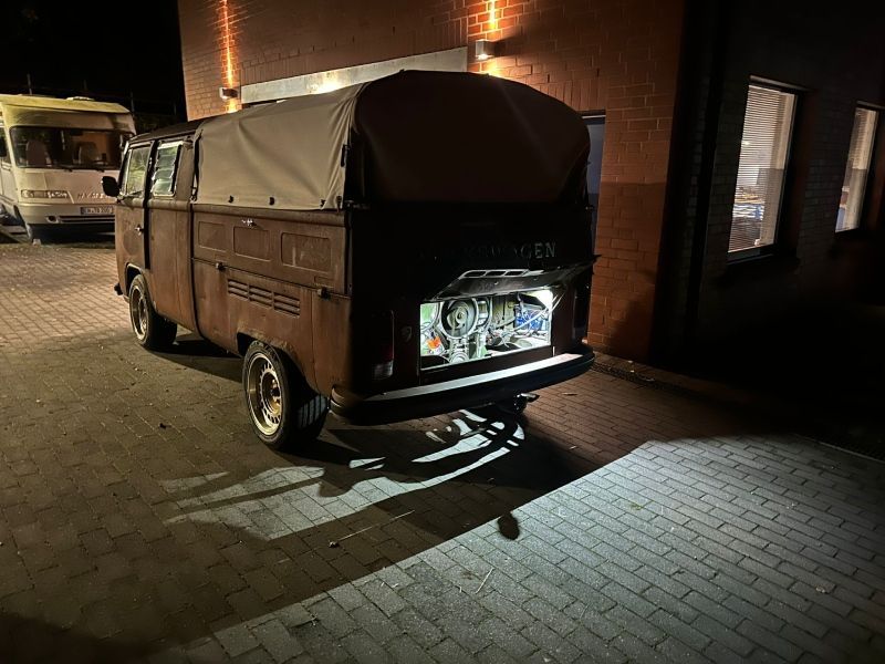 Ein dunkelbraunes, dreirädriges Lasten-Tuk-Tuk parkte nachts neben einem beleuchteten Backsteingebäude.