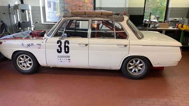 Ein weißer Oldtimer-Rennwagen mit der Nummer 36 steht in einer Werkstatt.