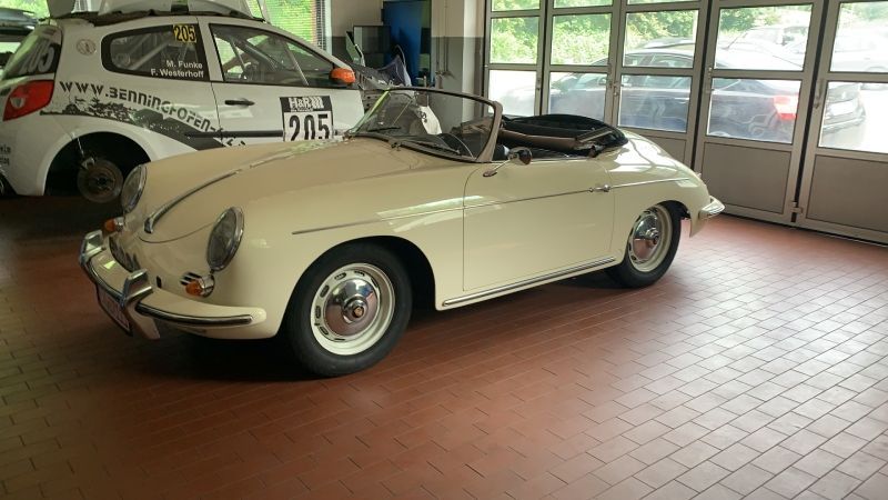 Ein cremefarbenes Oldtimer-Porsche-Coupé steht in einer Halle auf einem gefliesten Boden;