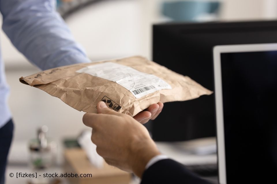 Eine Person übergibt einer anderen Person in der Nähe eines Computerbildschirms ein braunes Päckchen.