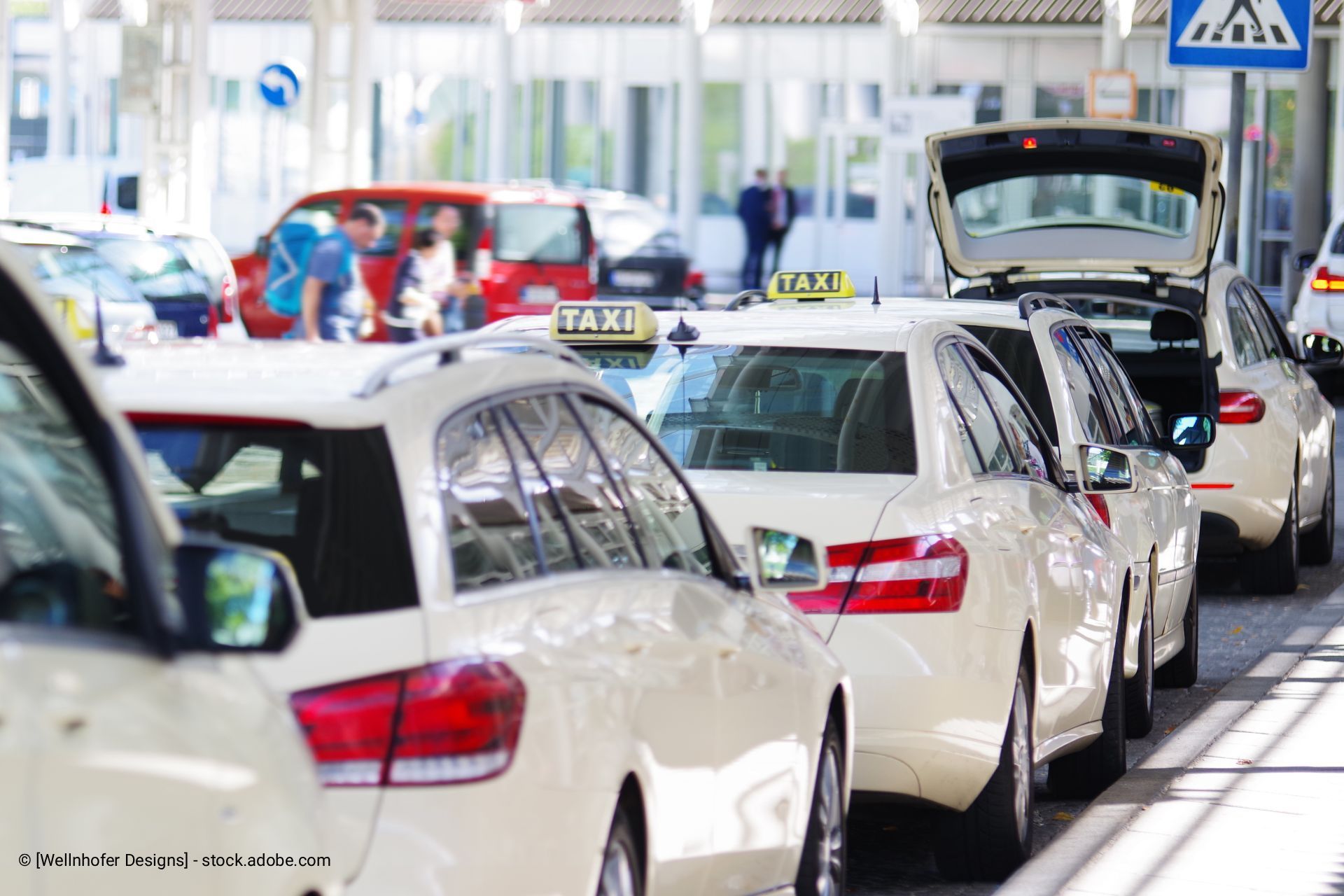 Vor einem Gebäude standen Taxis mit Fahrgästen in einer Reihe; einige waren weiß, alle hatten Taxilichter.