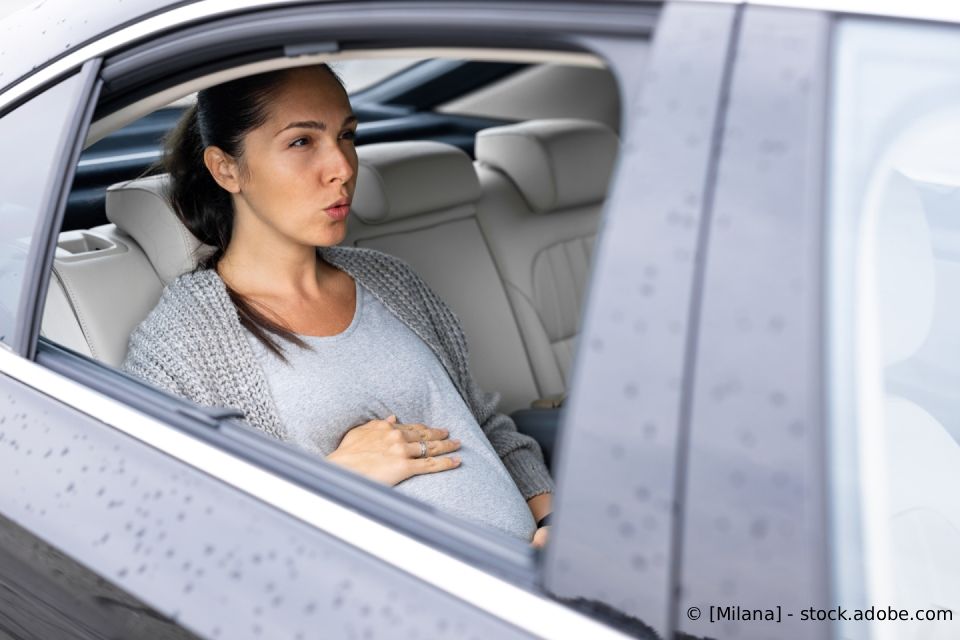 Schwangere Frau auf dem Rücksitz eines Autos, die sich den Bauch hält.