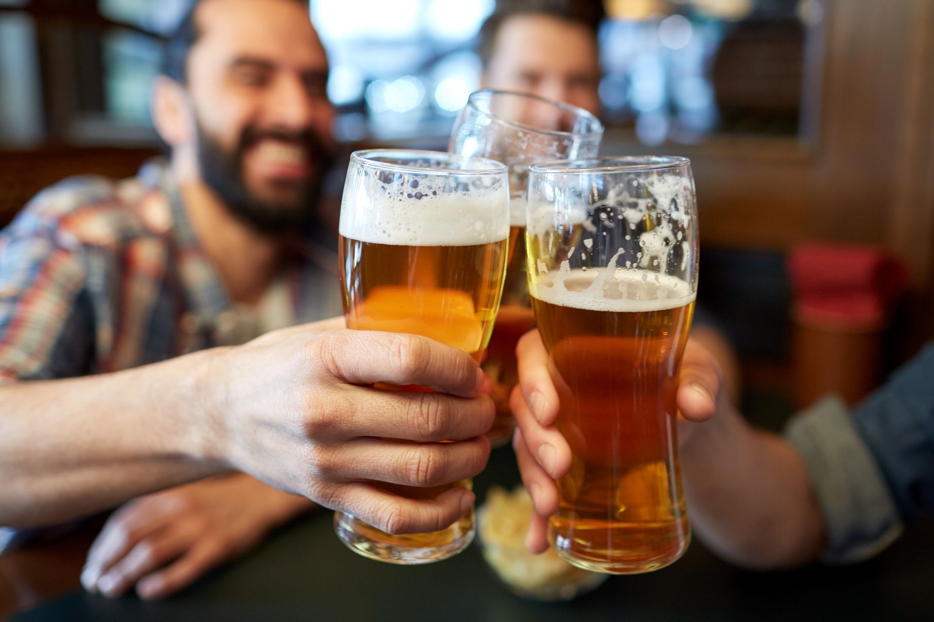 Trois personnes trinquent avec des verres de bière à une table, en souriant.