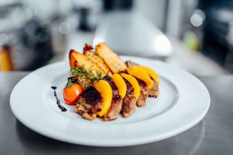 Assiette de tranches de viande cuite avec pêche, quartiers de pommes de terre et tomate.