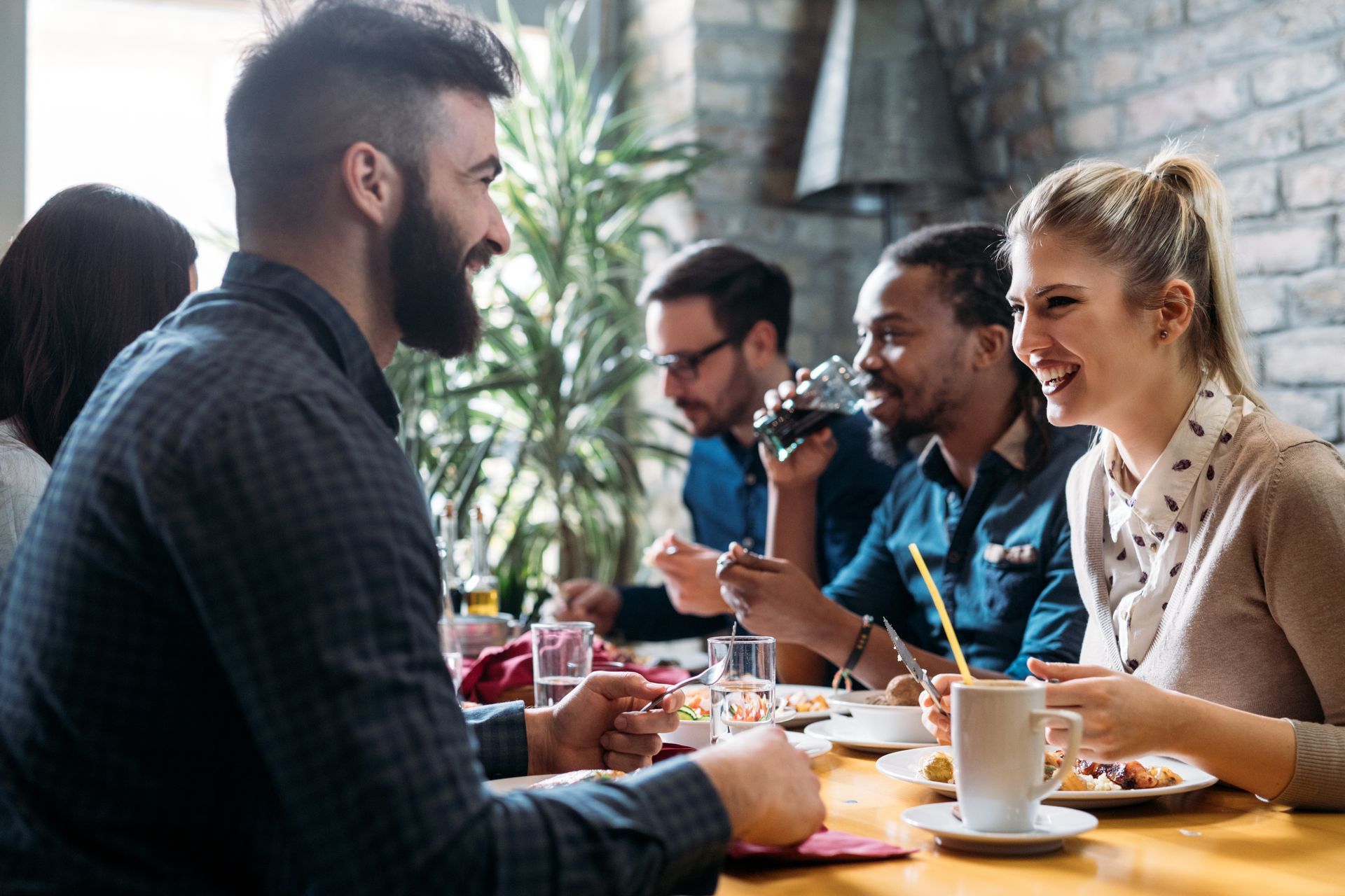 Des personnes attablées dans un restaurant, discutant et mangeant, devant un mur de briques.