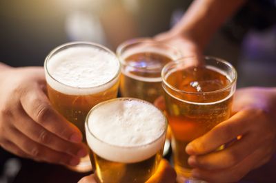 Quatre mains tenant des verres de bière, qui s'entrechoquent pour porter un toast.