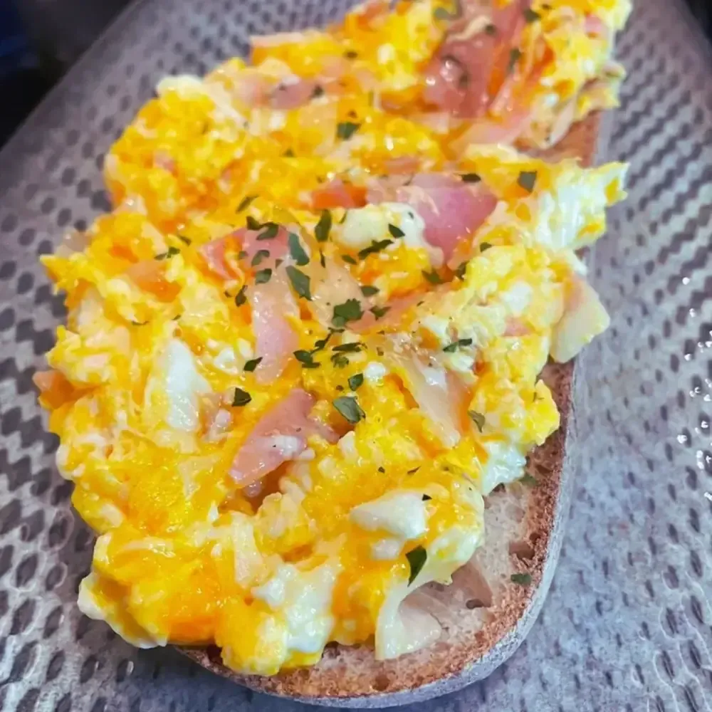Huevos revueltos con jamón y hierbas sobre tostadas.