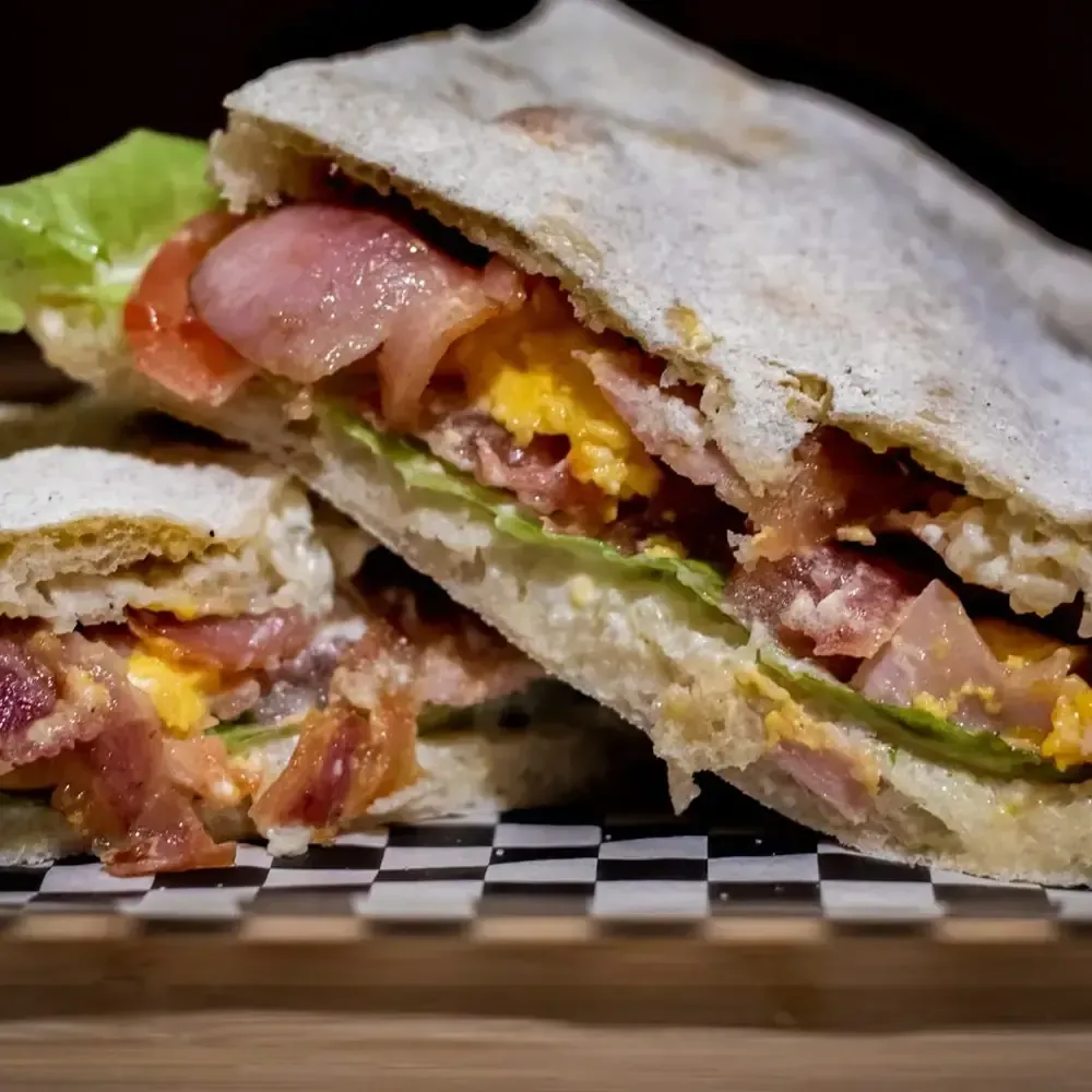 Sándwich cortado a la mitad con tocino, huevo, tomate y lechuga sobre una superficie cuadriculada.