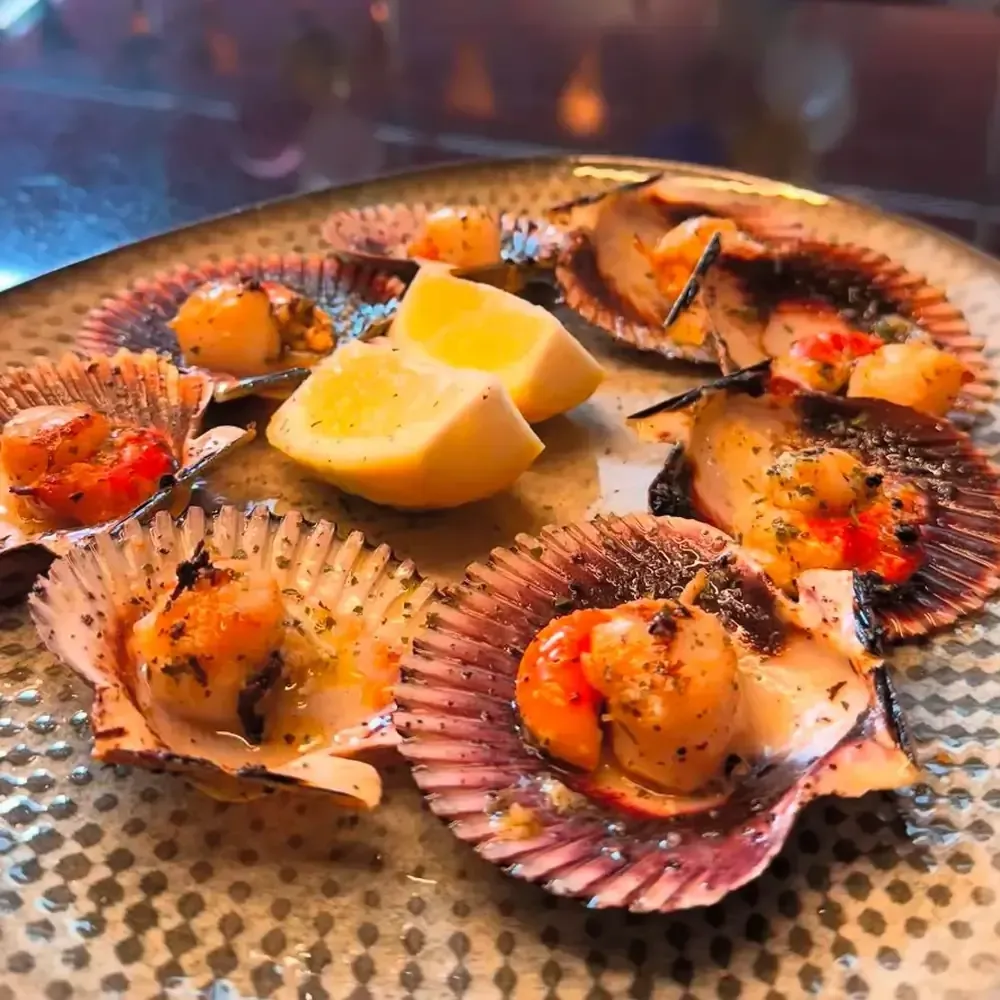Vieiras horneadas en conchas, adornadas con hierbas y gajos de limón, en un plato moteado.