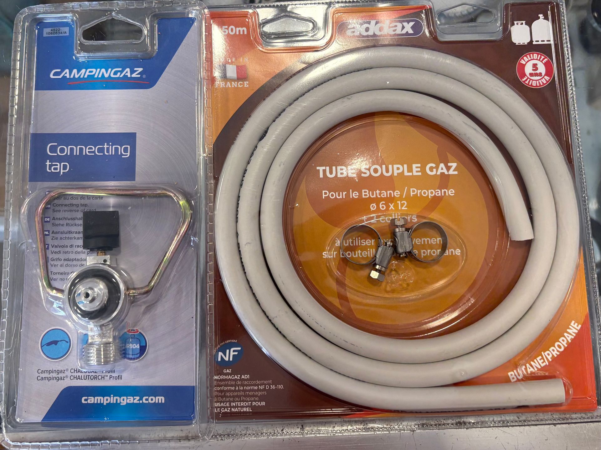 Deux accessoires à gaz pour le camping, emballés dans un emballage : un régulateur de cartouche de gaz et un tuyau de gaz.