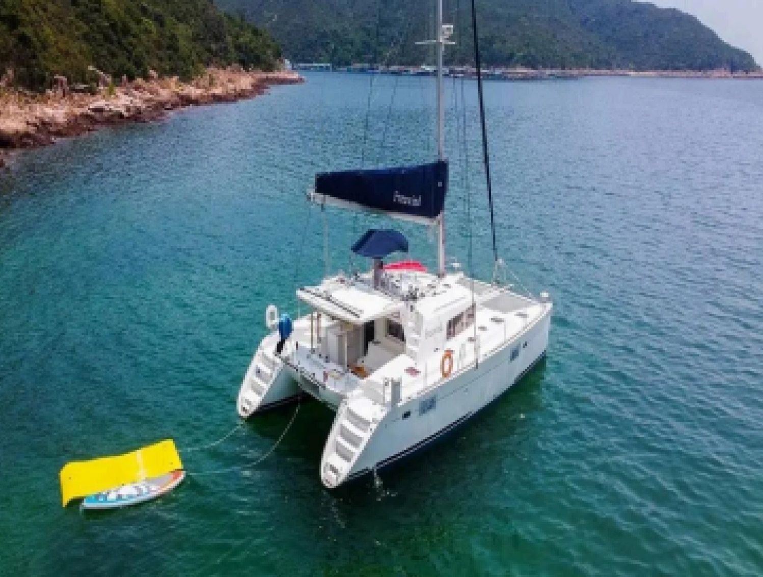 Un catamarán blanco anclado en aguas turquesas junto a una isla boscosa, con una boya amarilla cerca.