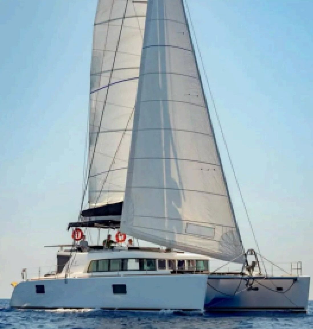 Catamarán blanco navegando sobre aguas azules en calma con las velas izadas bajo un cielo despejado.