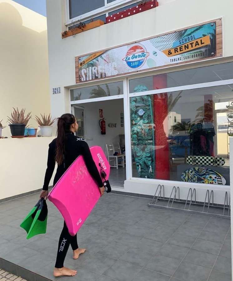 Una tabla de surf y unas aletas están delante de un cartel de surf de La Garita.