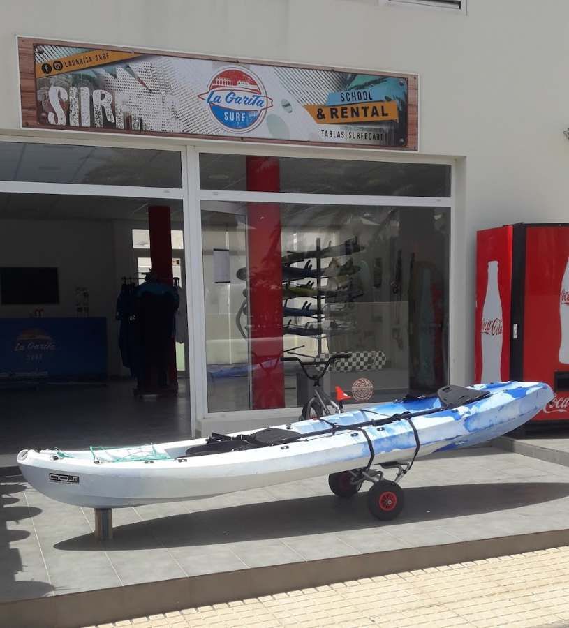 Una persona sosteniendo una tabla de surf frente a una tienda de surf.