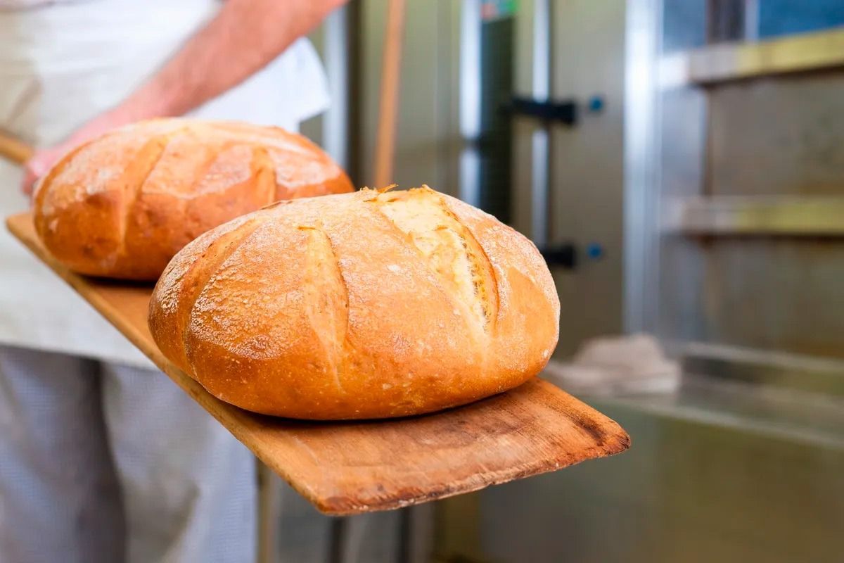 Un panadero sostiene dos hogazas de pan en una tabla de cortar de madera.