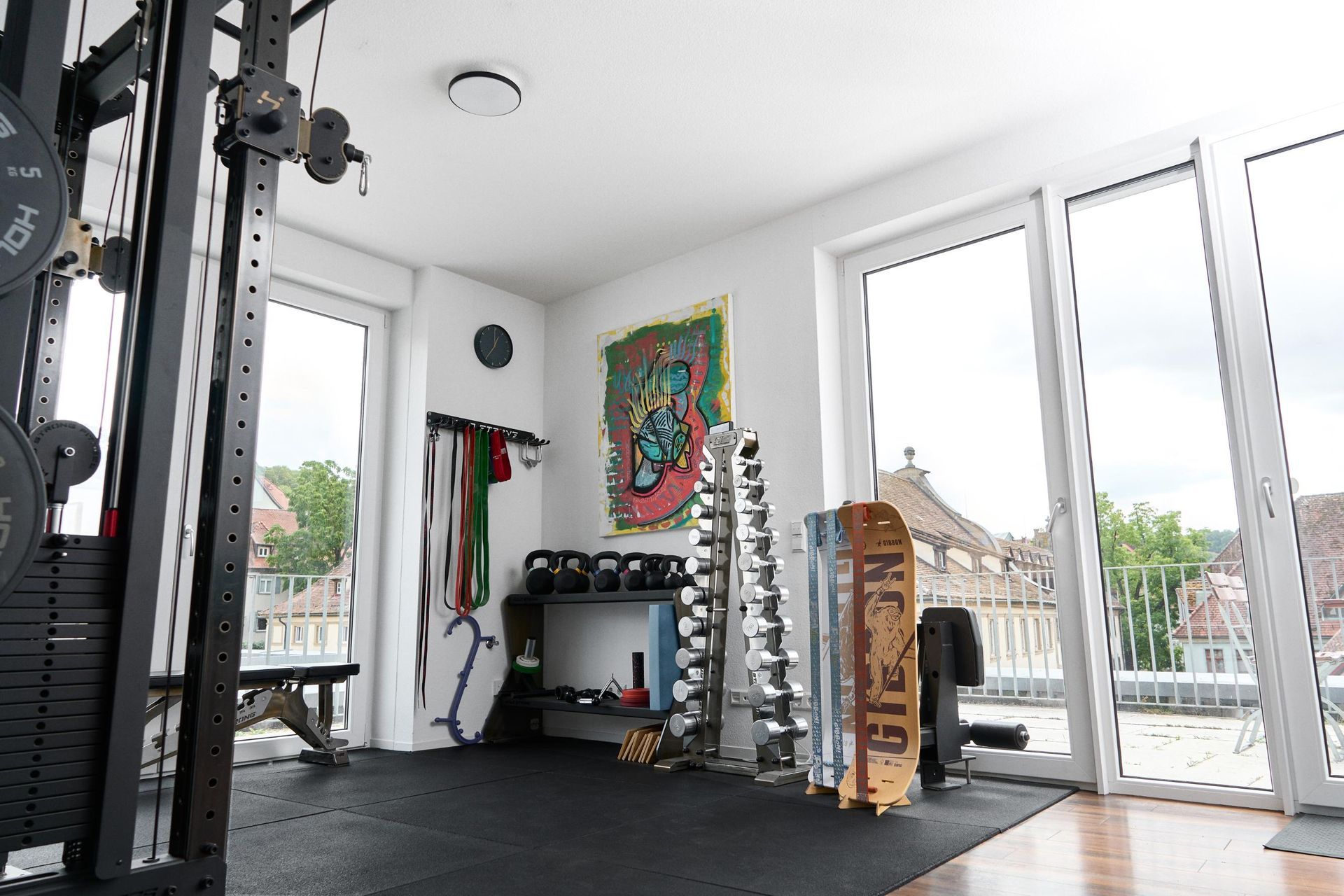 Heller Behandlungraum mit Hantelständer, Trainingsgeräten und großen Fenstern mit Blick auf einen Balkon