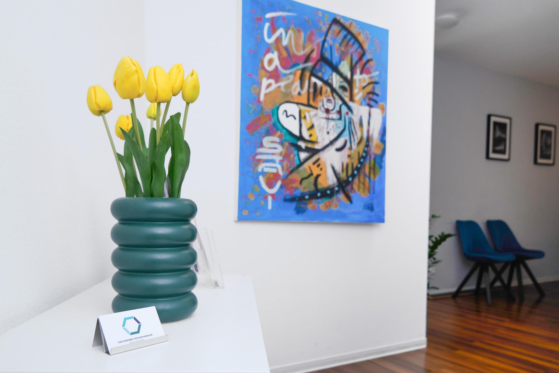 Gelbe Tulpen in einer petrolfarbenen Vase neben einem farbenfrohen abstrakten Gemälde in einem Wartebereich