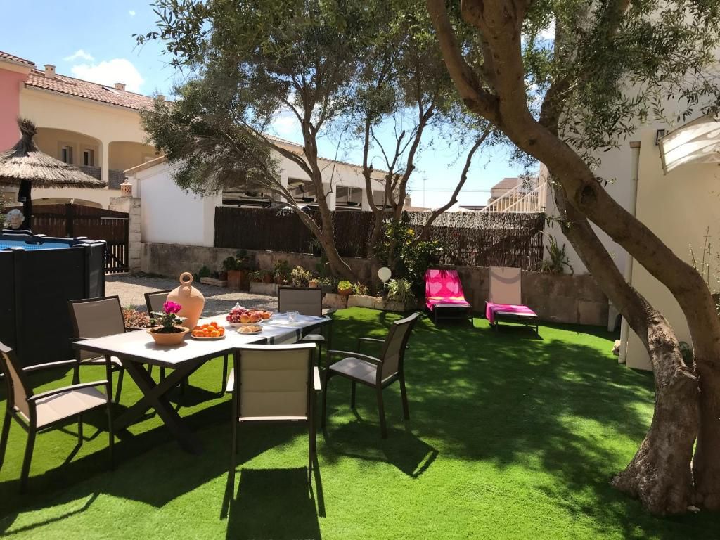 Patio trasero soleado con mesa, sillas y tumbonas de color rosa brillante bajo los árboles.
