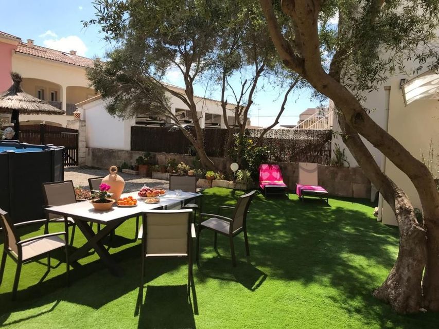 Patio trasero soleado con mesa, sillas y tumbonas de color rosa brillante bajo los árboles.