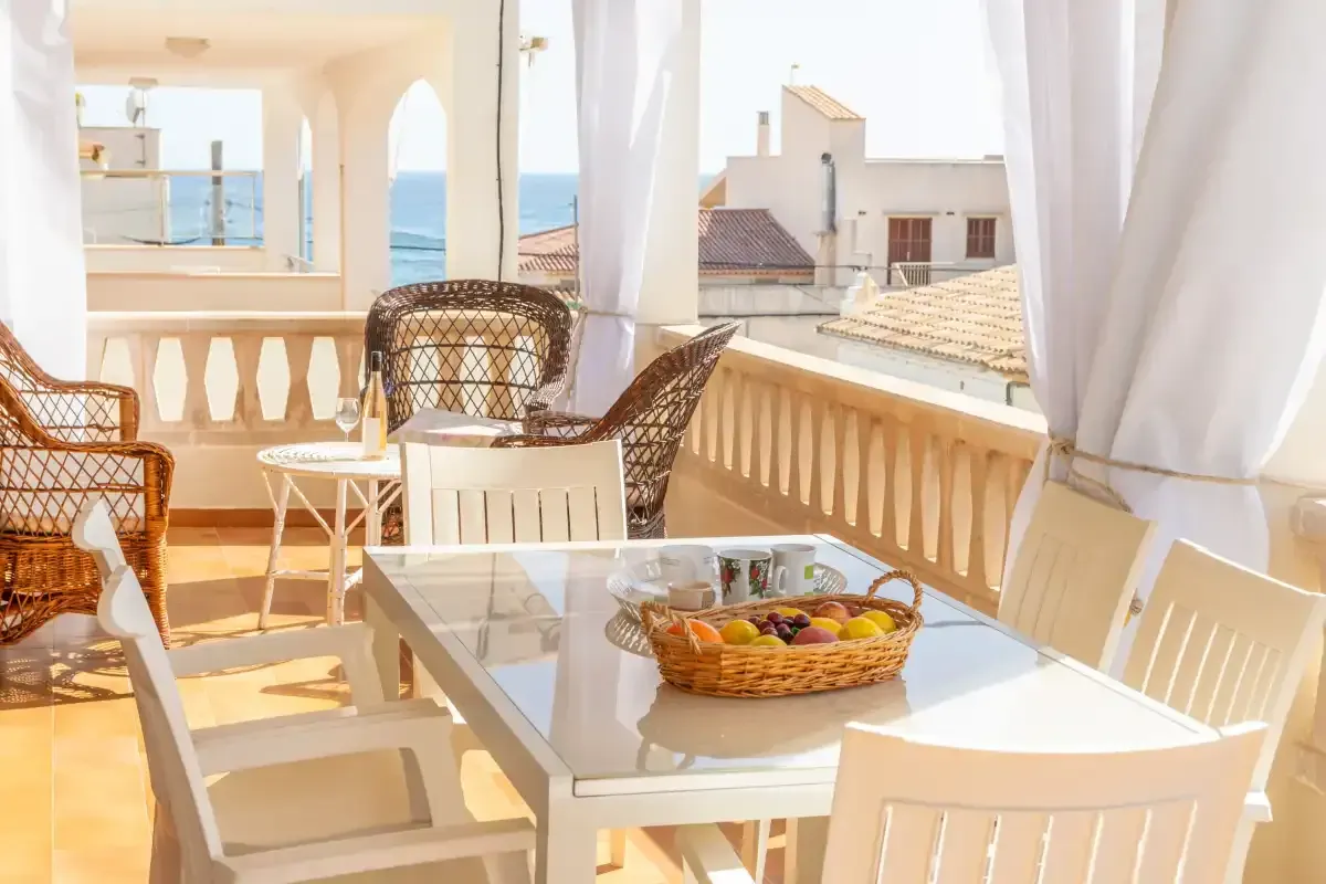 Terraza soleada en la azotea con muebles de mimbre blanco, mesa de cristal y vistas a la ciudad más allá de la barandilla.