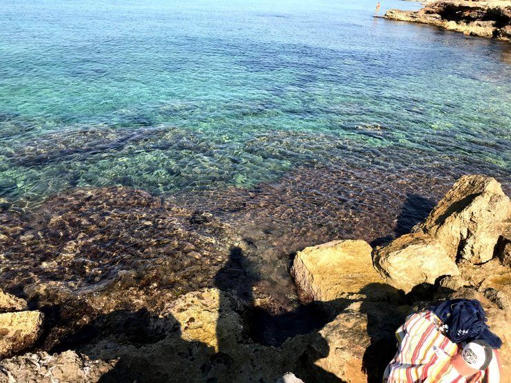 Aguas cristalinas de color azul marino sobre una costa rocosa, con una persona sentada.