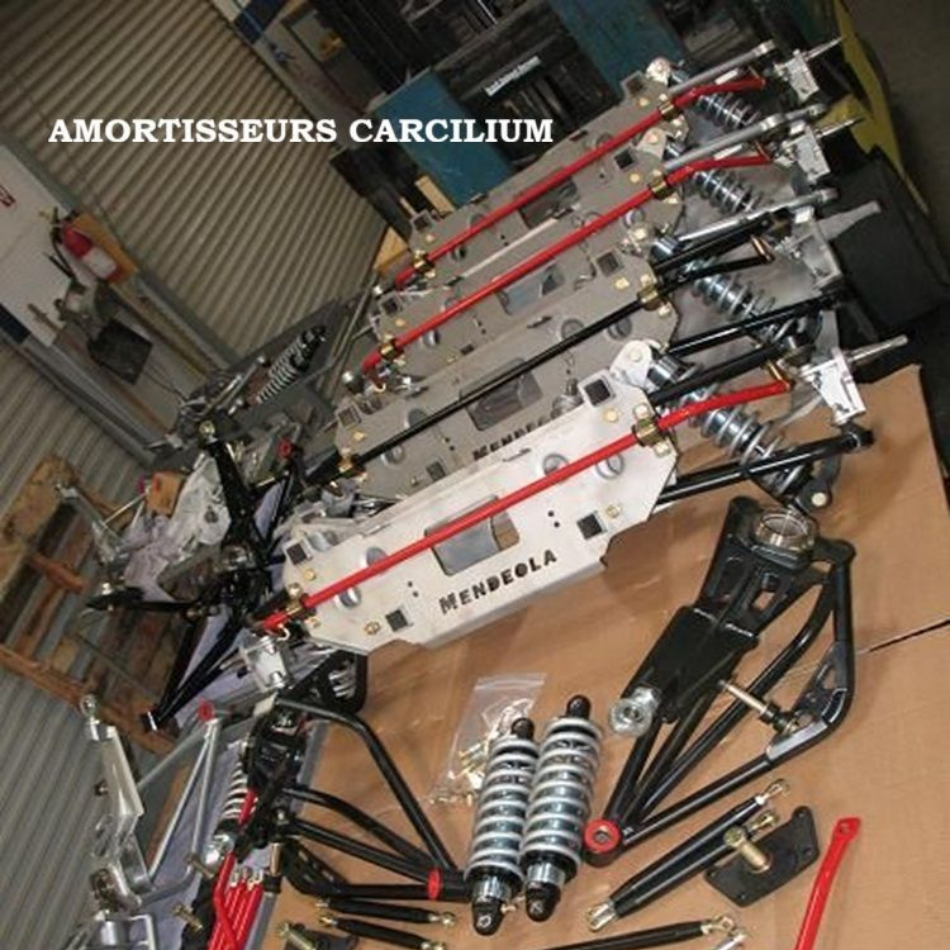 Pièces de suspension, notamment amortisseurs et bras de suspension, disposées sur une surface. Composants noirs, rouges et argentés.