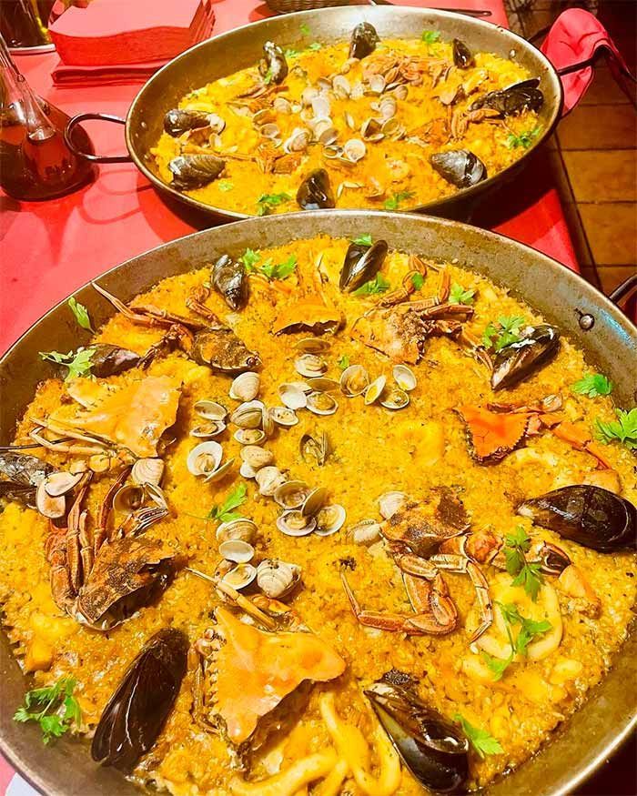 Sobre una mesa roja hay dos sartenes de paella.