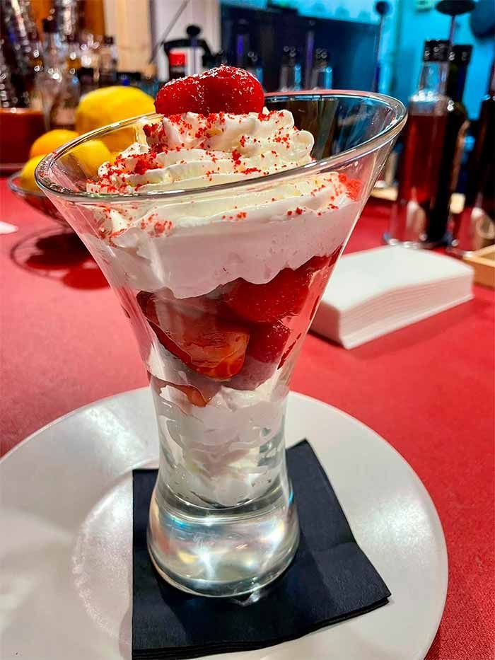 Una copa de martini llena de fresas y crema batida en un plato.
