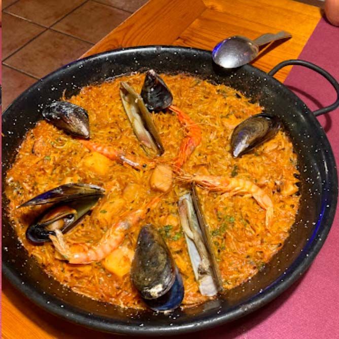 Una olla de comida con camarones, mejillones y arroz.