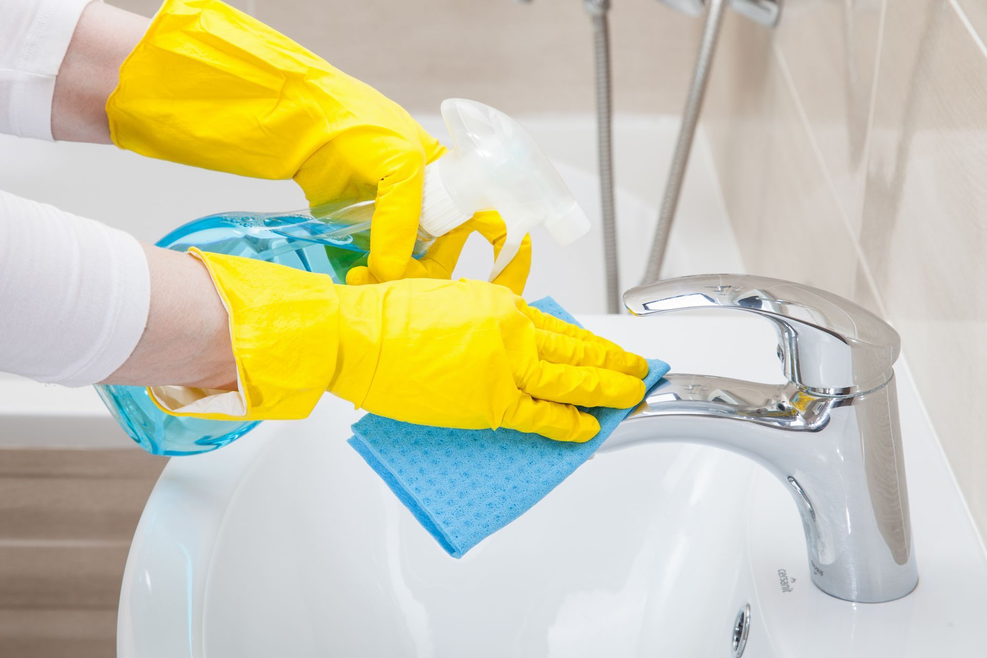 Une personne portant des gants jaunes nettoie un lavabo de salle de bain avec un chiffon.