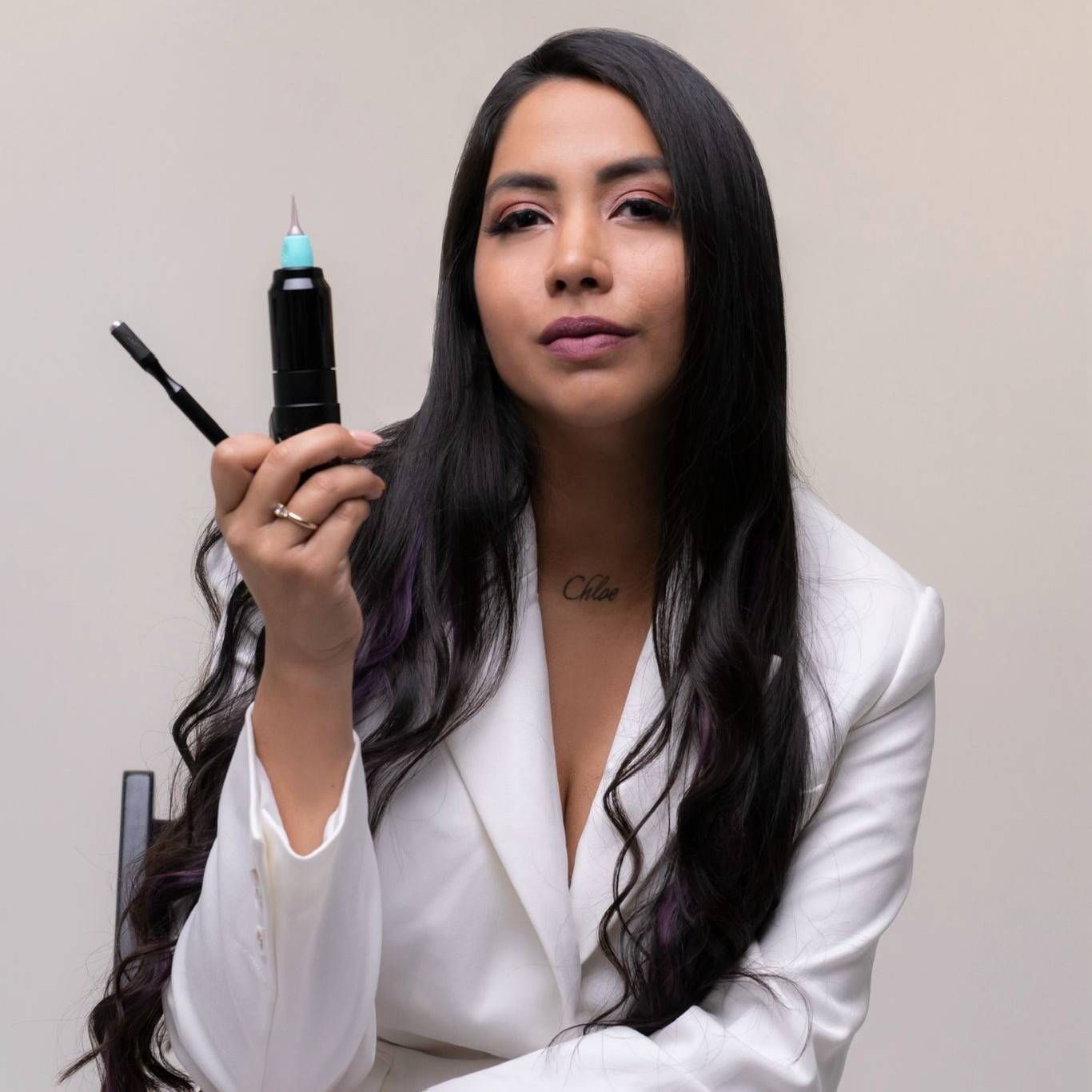 Mujer con chaqueta blanca sosteniendo un vaporizador y un cartucho, sentada sobre un fondo liso.