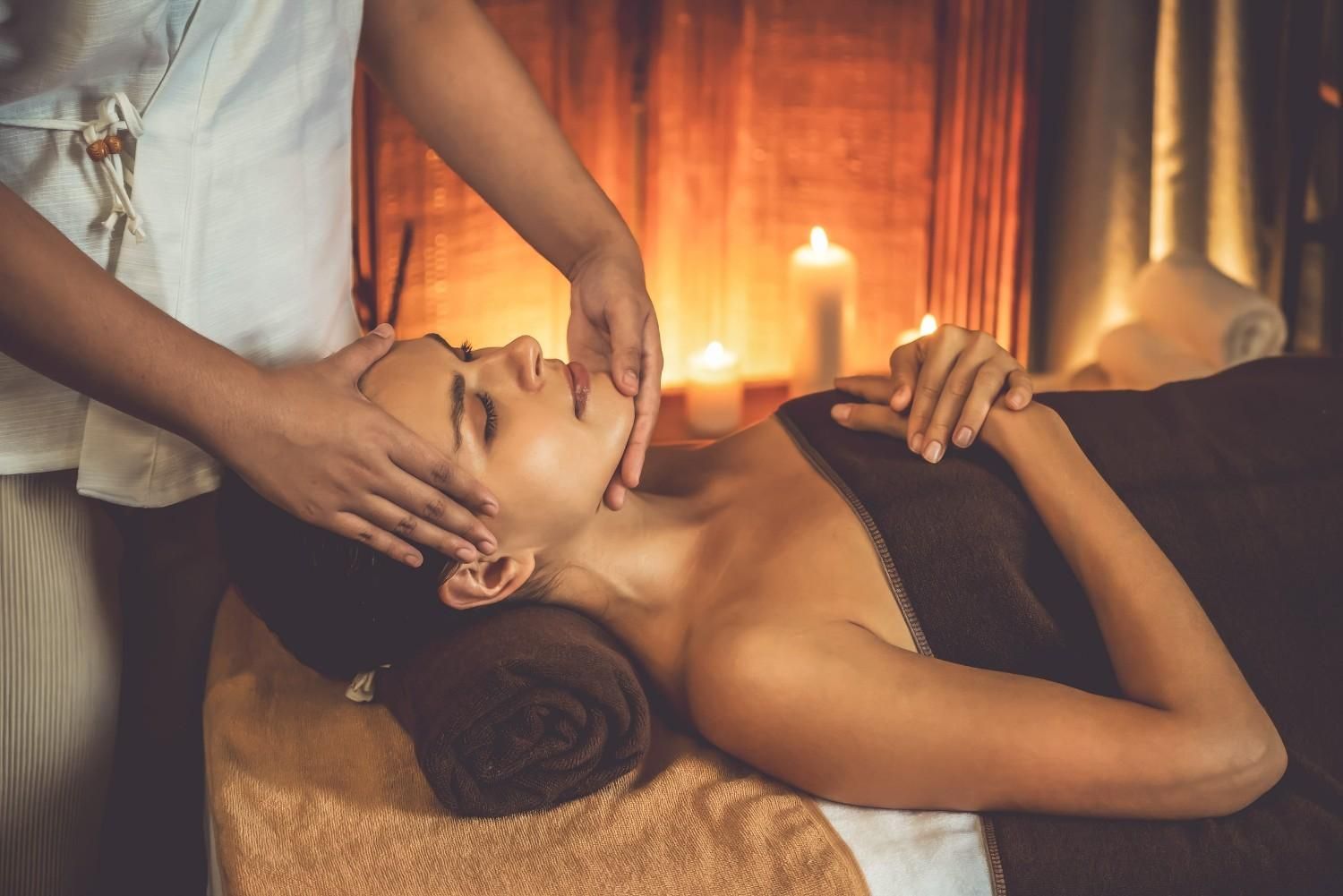 Una terapeuta de spa le da un masaje facial a una clienta recostada a la luz de las velas.
