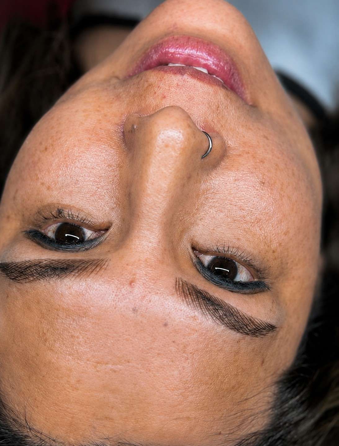Primer plano invertido del rostro de una persona con maquillaje oscuro en los ojos y un piercing en la nariz.