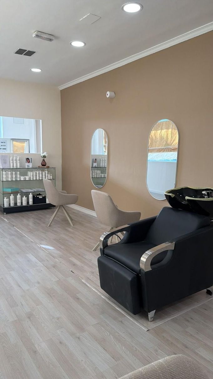 Interior de salón moderno con paredes beige, sillón de peluquería negro, espejos y estantes para productos.