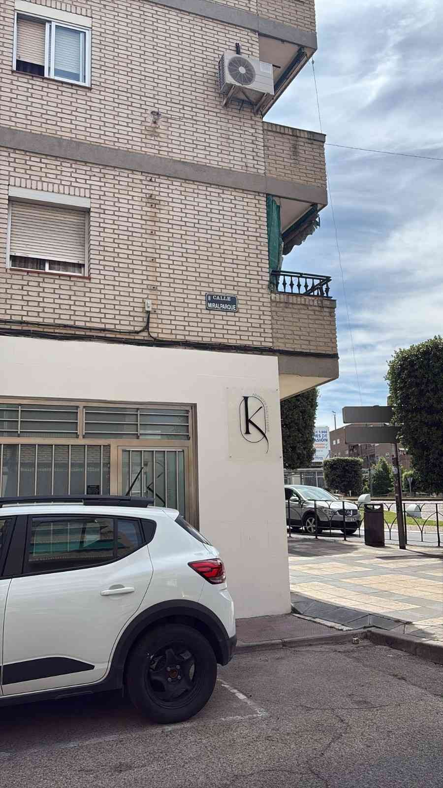 Un SUV blanco estacionado junto a un edificio de apartamentos con azulejos beige en una calle tranquila.