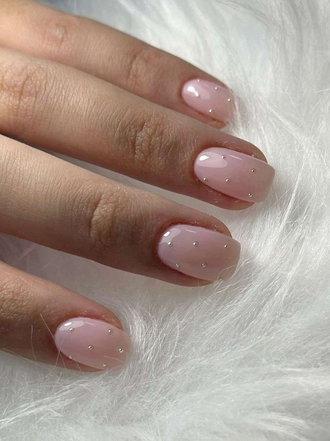 Mano con manicura rosa pálido brillante y pequeños puntos blancos sobre un fondo de suave pelo blanco.