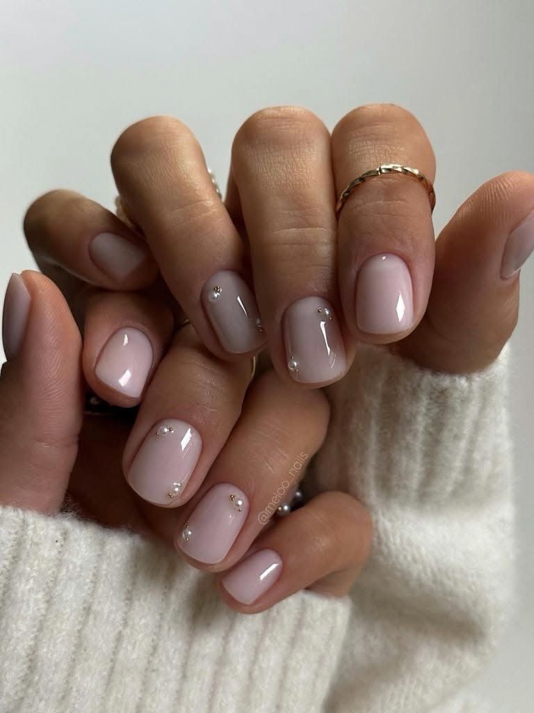 Manos con manicura rosa nude brillante y un anillo de oro, envueltas en un suéter color crema.