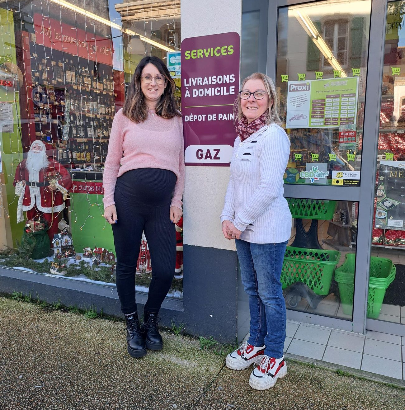 Deux femmes se tiennent devant la vitrine d'un magasin. La vitrine est décorée pour les fêtes. 