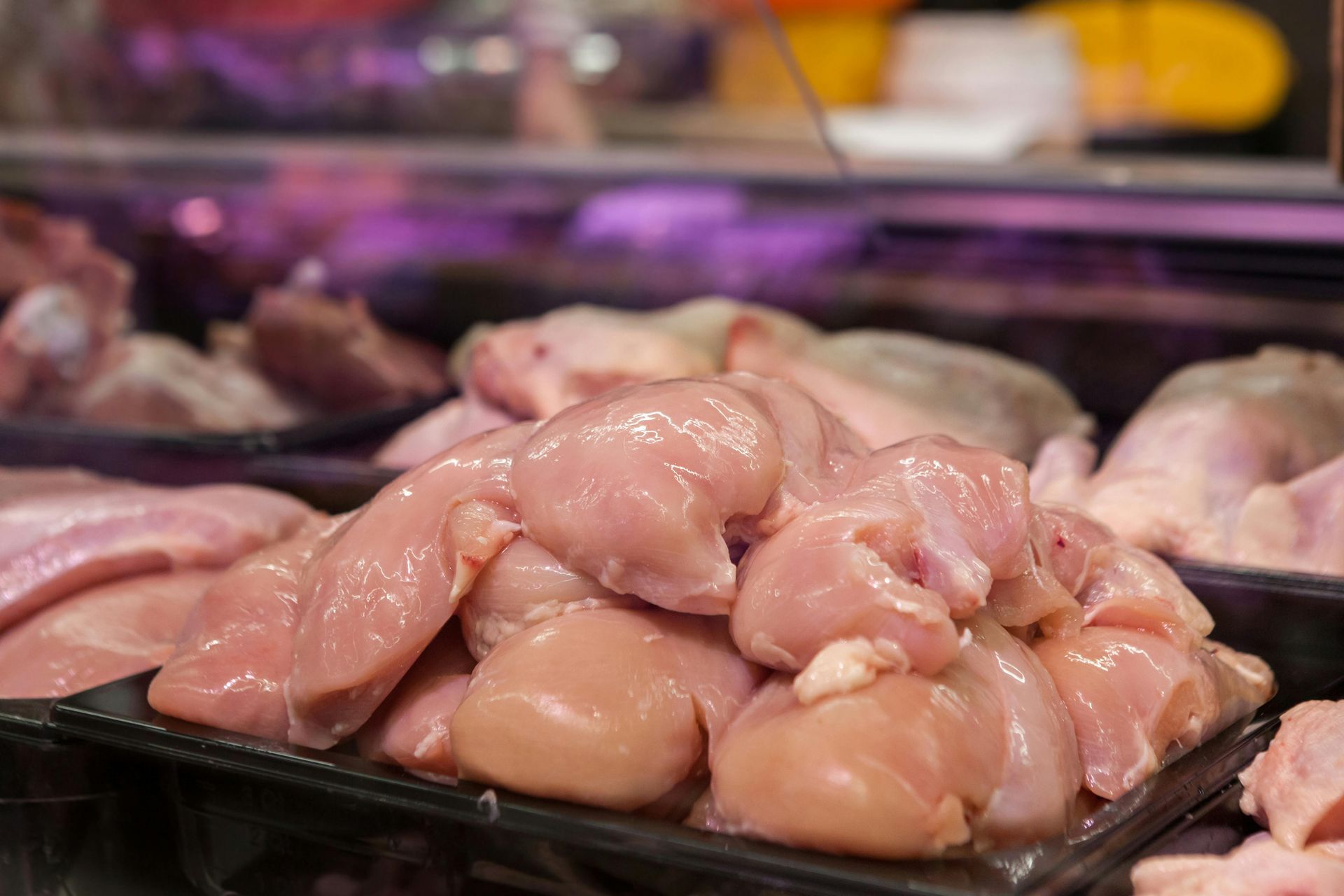 Des morceaux de poulet cru sont exposés sur un comptoir de viande dans un magasin, éclairés par des lumières zénithales.