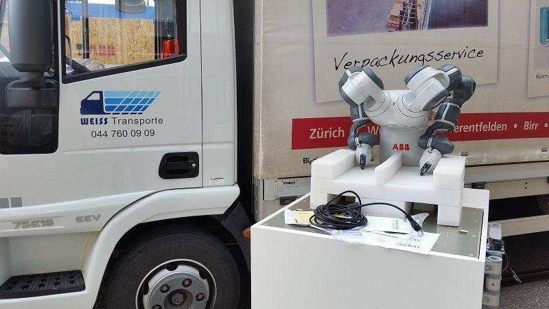 Ein Roboter sitzt auf einem Tisch neben einem Lkw. Foto von der Weiss Transporte AG.