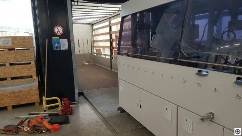 Eine grosse weisse Maschine steht in einer Lagerhalle neben einer Holzkiste. Foto von der Weiss Transporte AG.