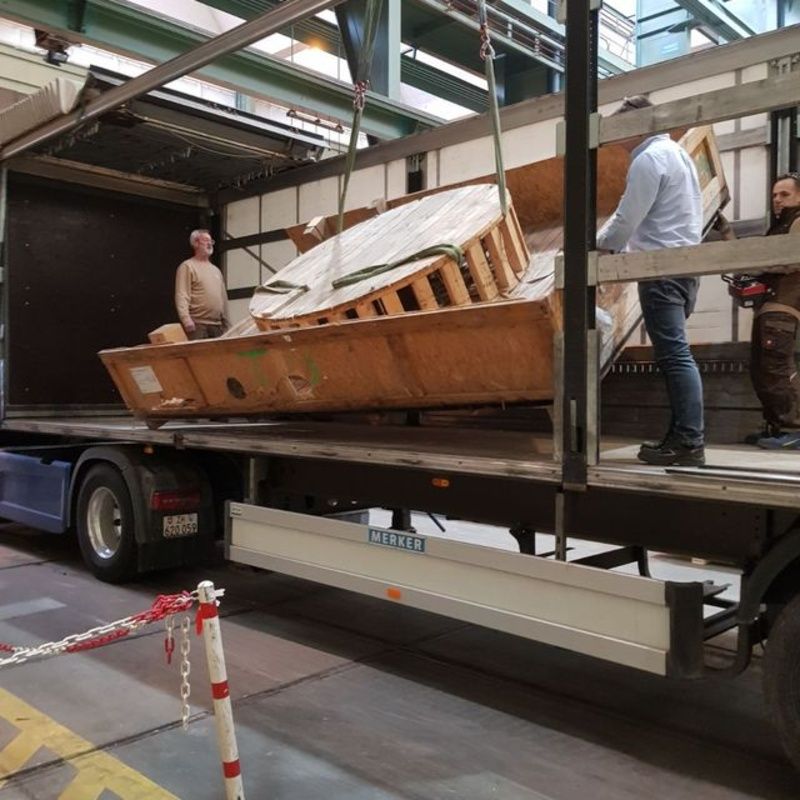 Eine grosse Holzkiste wird von der Ladefläche eines Lkws gehoben. Foto von der Weiss Transporte AG.