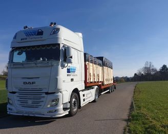Ein weisser Lastwagen fährt eine Strasse neben einem Feld entlang. Foto von der Weiss Transporte AG.