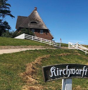 Vor einem Reetdachhaus steht ein Schild mit der Aufschrift „Kirchwart“.
